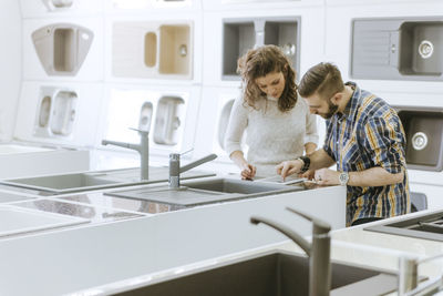 Customers consulting saleswoman in shop for kitchen sinks