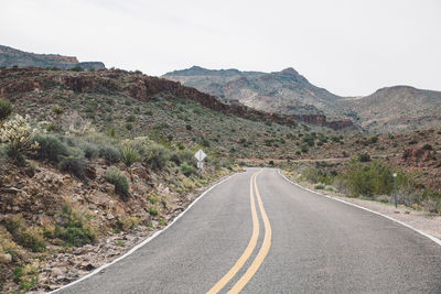 Empty road by mountains against clear sky