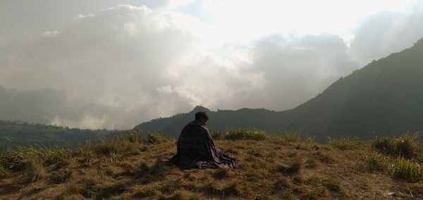 Rear view of man sitting on mountain against sky
