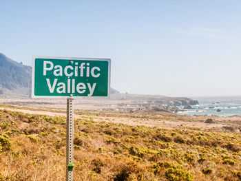 Road sign by sea against sky