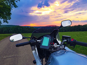 Close-up of motorcycle on road against sky during sunset