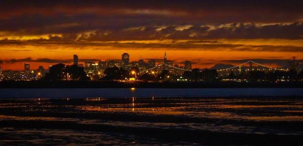 Bay bridge over sea against sky during sunset in city