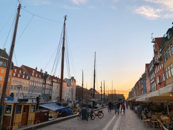 Sailboats in city by buildings against sky during sunset