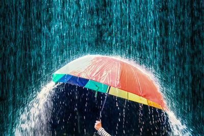 Cropped hand holding umbrella during rainfall