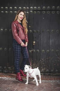 Portrait of happy young woman standing with dog at doorway