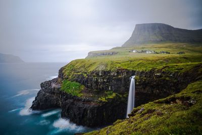 Scenic view of mountain and sea against cloudy sky at faroe islands
