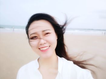 Portrait of smiling young woman on beach against sky