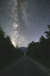 Scenic view of road amidst trees against sky at night