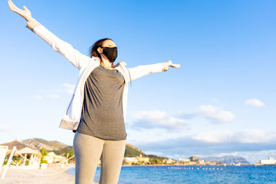 Woman with arms raised standing against sky