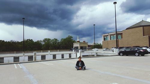 Teenage boy sitting on floor against cloudy sky
