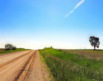 Road passing through field against cloudy sky