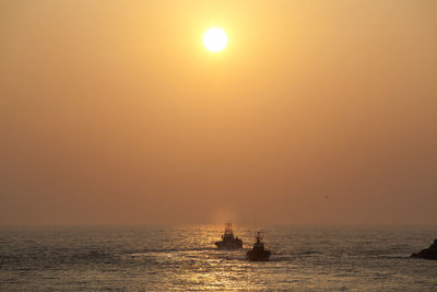 Silhouette boat sailing on sea against orange sky