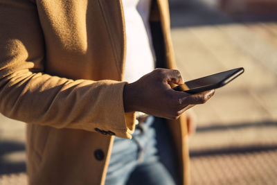 Crop of anonymous young african american male in trendy outfit on street and browsing mobile phone on sunny summer day