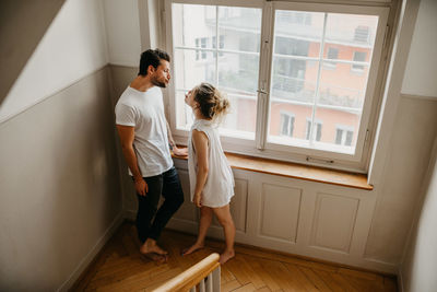 Rear view of friends standing against window at home