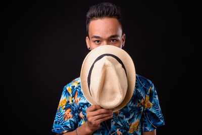 Portrait of young man holding mask against black background