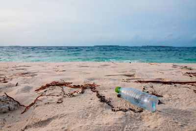 Water bottle on sand at beach against sky