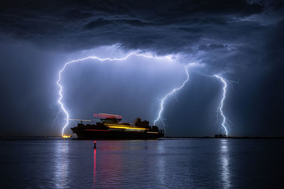 Sailing container ship below dramatic lightning storm