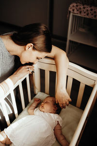 The child sleeps in a crib, the mother sits next to her and tenderly looks at her daughter