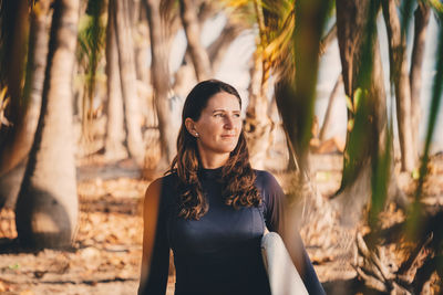 Thoughtful mature woman with surfboard at beach