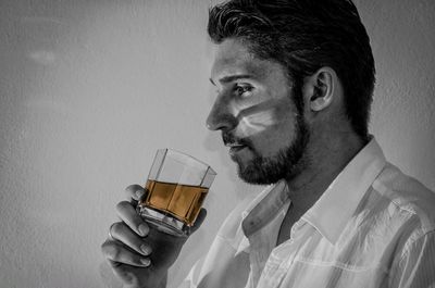 Portrait of young man drinking glass against white background