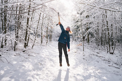 Full length of woman jumping while playing with trees on snow covered land