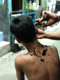 Cropped hands of barber cutting shirtless boy hair outdoors