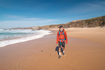 Rear view of woman walking at beach against sky