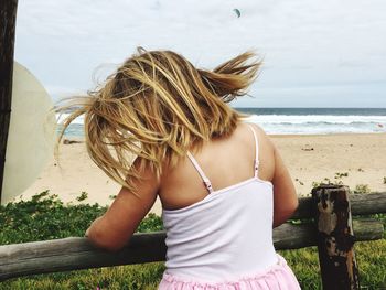 Rear view of young woman at beach against sky