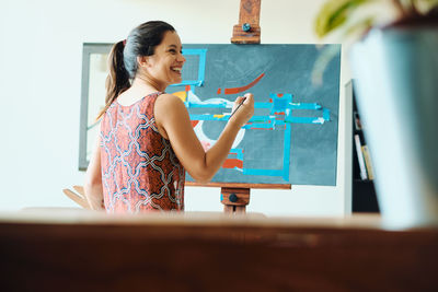 Rear view of smiling woman painting on easel