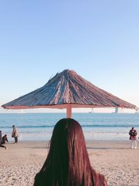 Rear view of woman standing on beach against clear sky