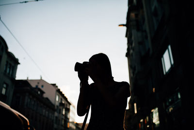 Silhouette man photographing on city against sky