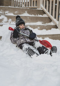 Portrait of boy with shovel lying on snowy steps