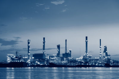 Illuminated factory by sea against sky at night