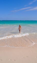 Young woman in bikini walking at beach against sky