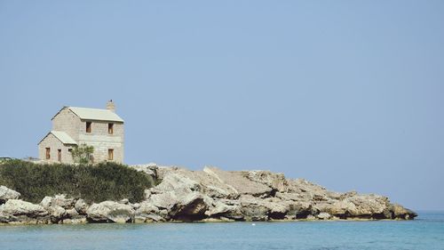 Lighthouse on cliff by sea against clear sky