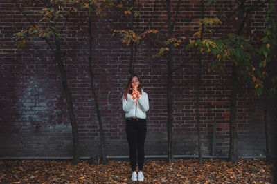 Portrait of young woman standing against brick wall