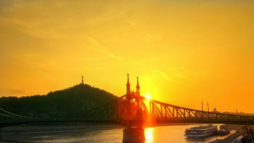 Liberty bridge over danube river against orange sunset sky