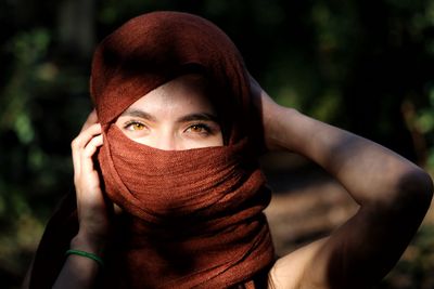 Close-up portrait of young woman hiding face outdoors