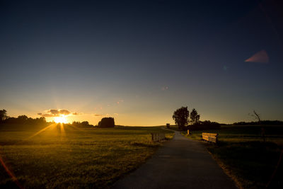 Road amidst field against sky during sunset