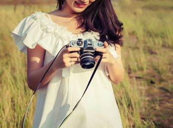 Midsection of young woman holding camera on field