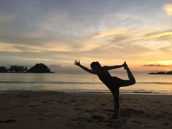 Silhouette of woman exercising at beach against sky during sunset