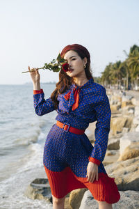 Close-up portrait of beautiful woman holding rose standing at beach