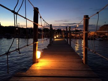 Illuminated footbridge over sea during dusk