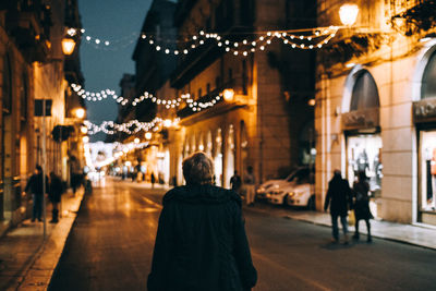 Rear view of woman walking on illuminated street at night