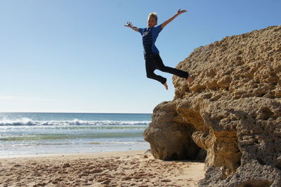 Woman jumping on beach against clear sky