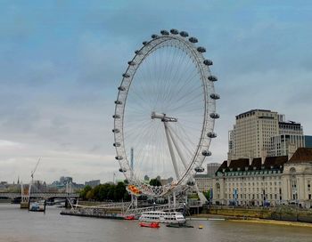 Ferris wheel by river against sky in city