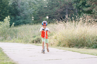 Little boy in sports helmet riding scooter on road street in park on summer day. seasonal activities 