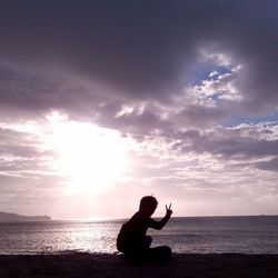 Silhouette woman sitting on beach against sky during sunset