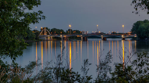 Scenic view of bridge over body of water or river with lights reflecting on the water at sunset