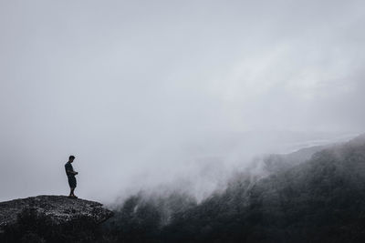 Side view of man standing on mountain against cloudy sky